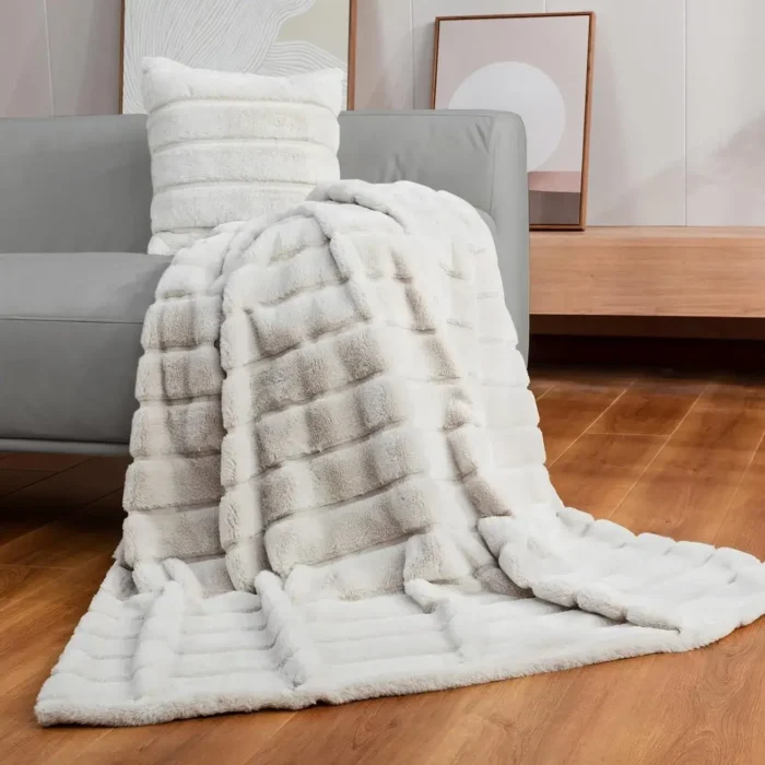 A plush grey Cozy Bliss Faux Fur Throw Blanket draped over a stylish armchair, showing off its ultra-soft, reversible texture in a cozy living room setting.