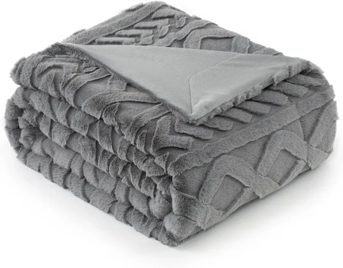 A plush grey Cozy Bliss Faux Fur Throw Blanket draped over a stylish armchair, showing off its ultra-soft, reversible texture in a cozy living room setting.